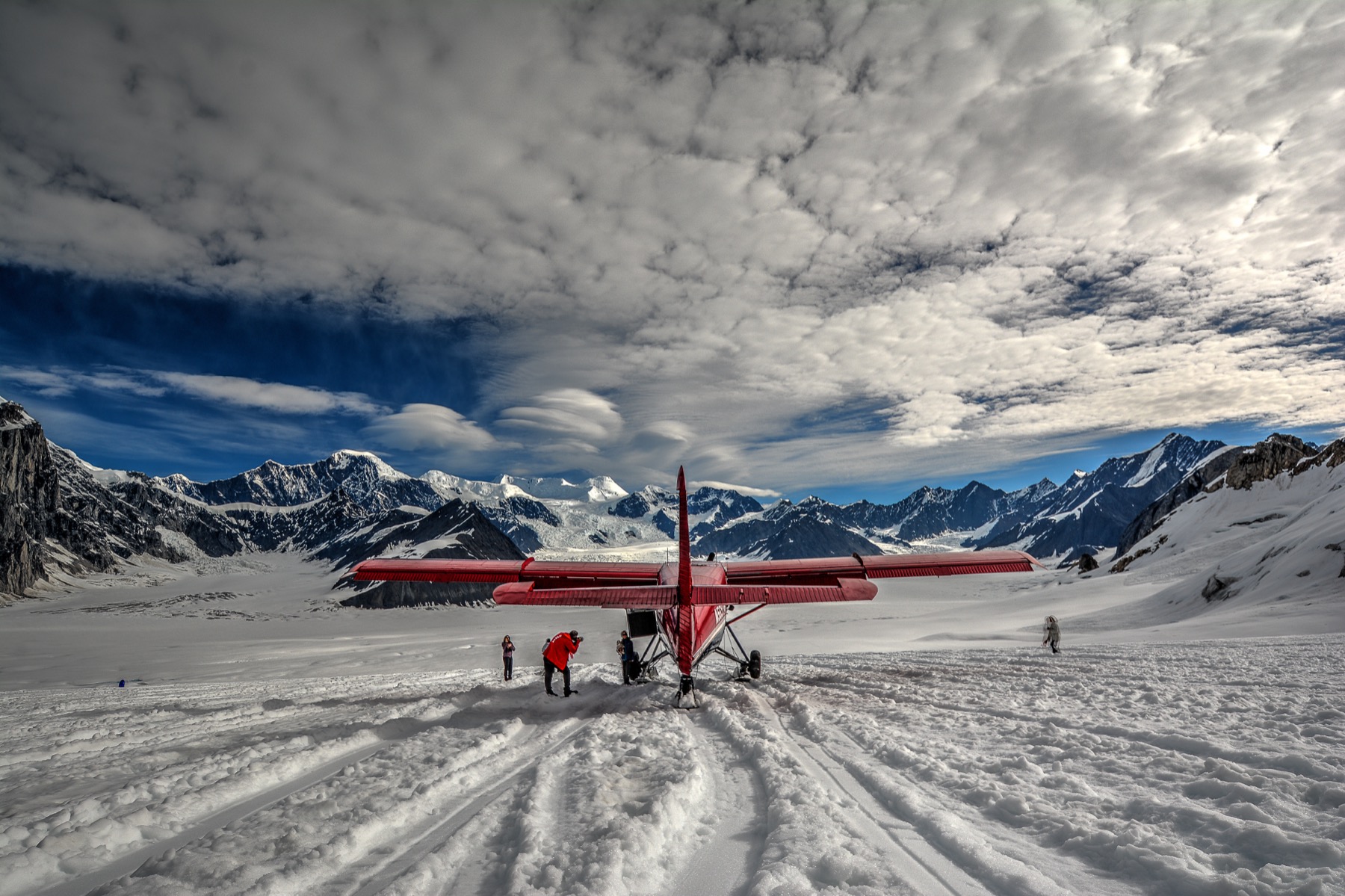 Ski-equipped tour plane parked on a glacier with passengers photographing the mountains